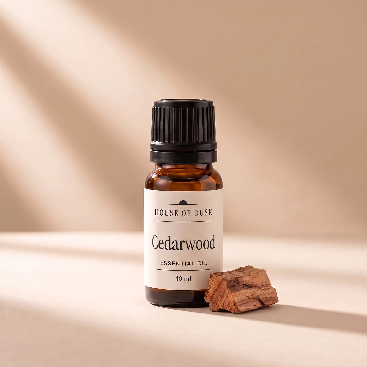 Cedarwood essential oil in a 10 ml amber glass bottle with a House of Dusk label, beside a small rough piece of reddish brown cedar wood