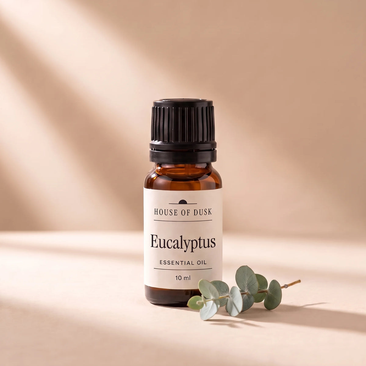 Eucalyptus essential oil in a 10 ml amber glass bottle with a House of Dusk label, beside a small sprig of silver green eucalyptus leaves