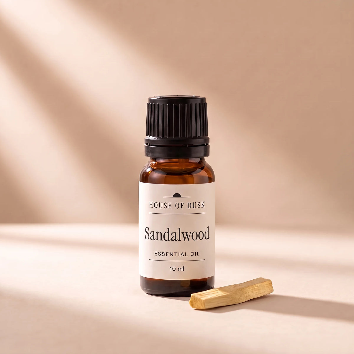 Sandalwood essential oil in a 10 ml amber glass bottle with a House of Dusk label, beside a small piece of pale golden sandalwood