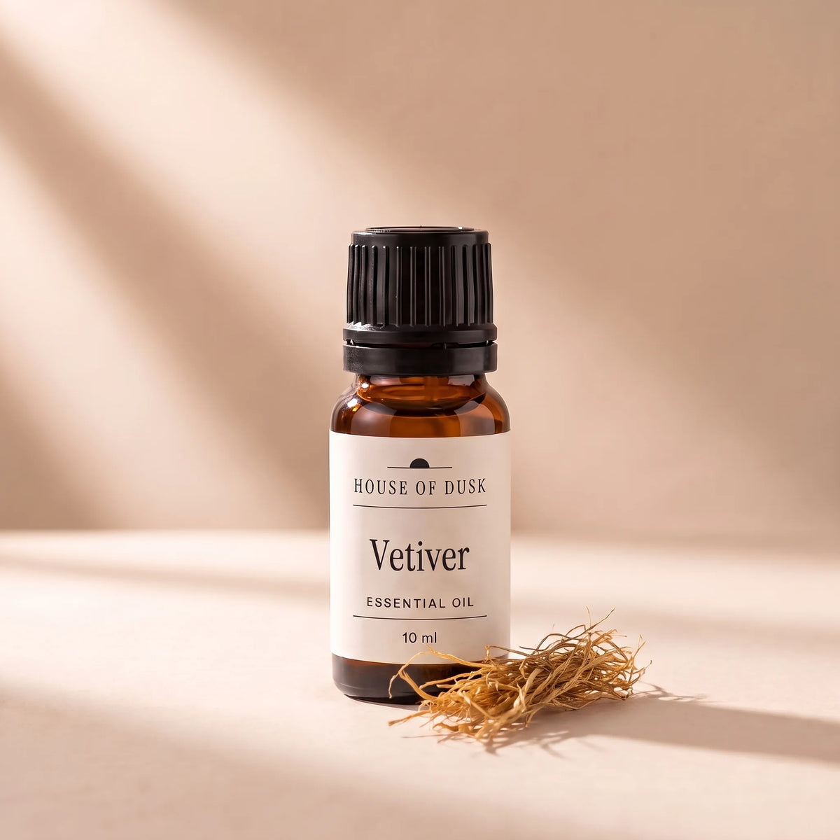Vetiver essential oil in a 10 ml amber glass bottle with a House of Dusk label, beside a small tuft of dried golden vetiver roots