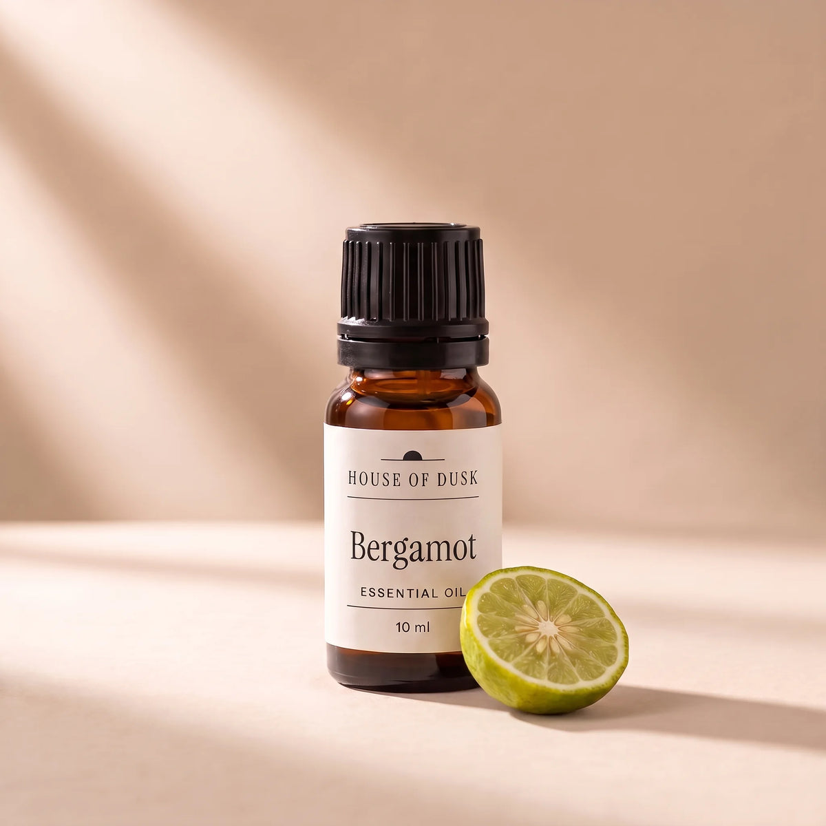 Bergamot essential oil in a 10 ml amber glass bottle with a House of Dusk label, beside half of a small green yellow bergamot orange