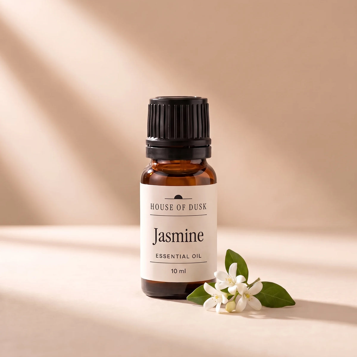 Jasmine essential oil in a 10 ml amber glass bottle with a House of Dusk label, beside a small sprig of white jasmine flowers with two leaves