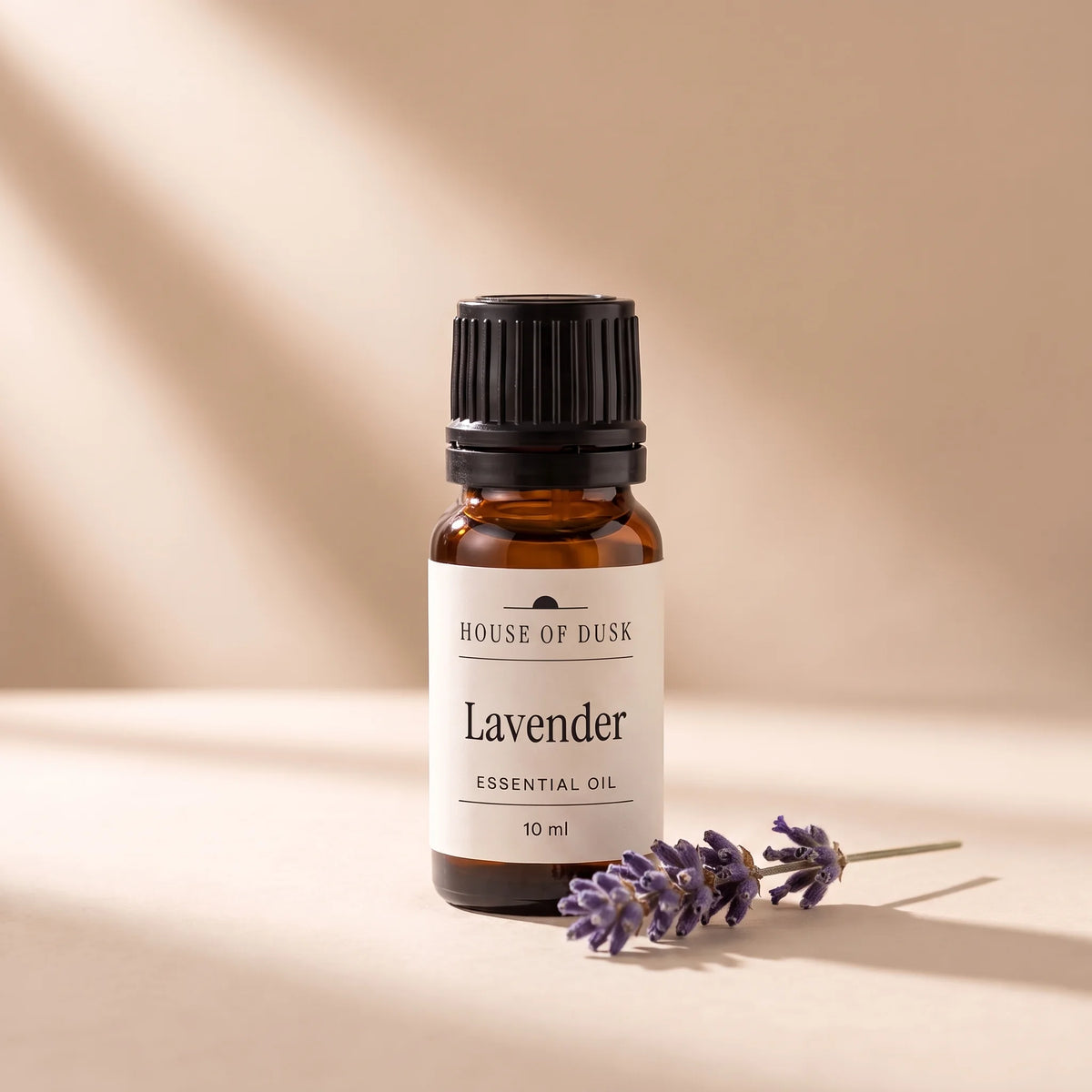 Lavender essential oil in a 10 ml amber glass bottle with a House of Dusk label, beside a small sprig of dried purple lavender flowers