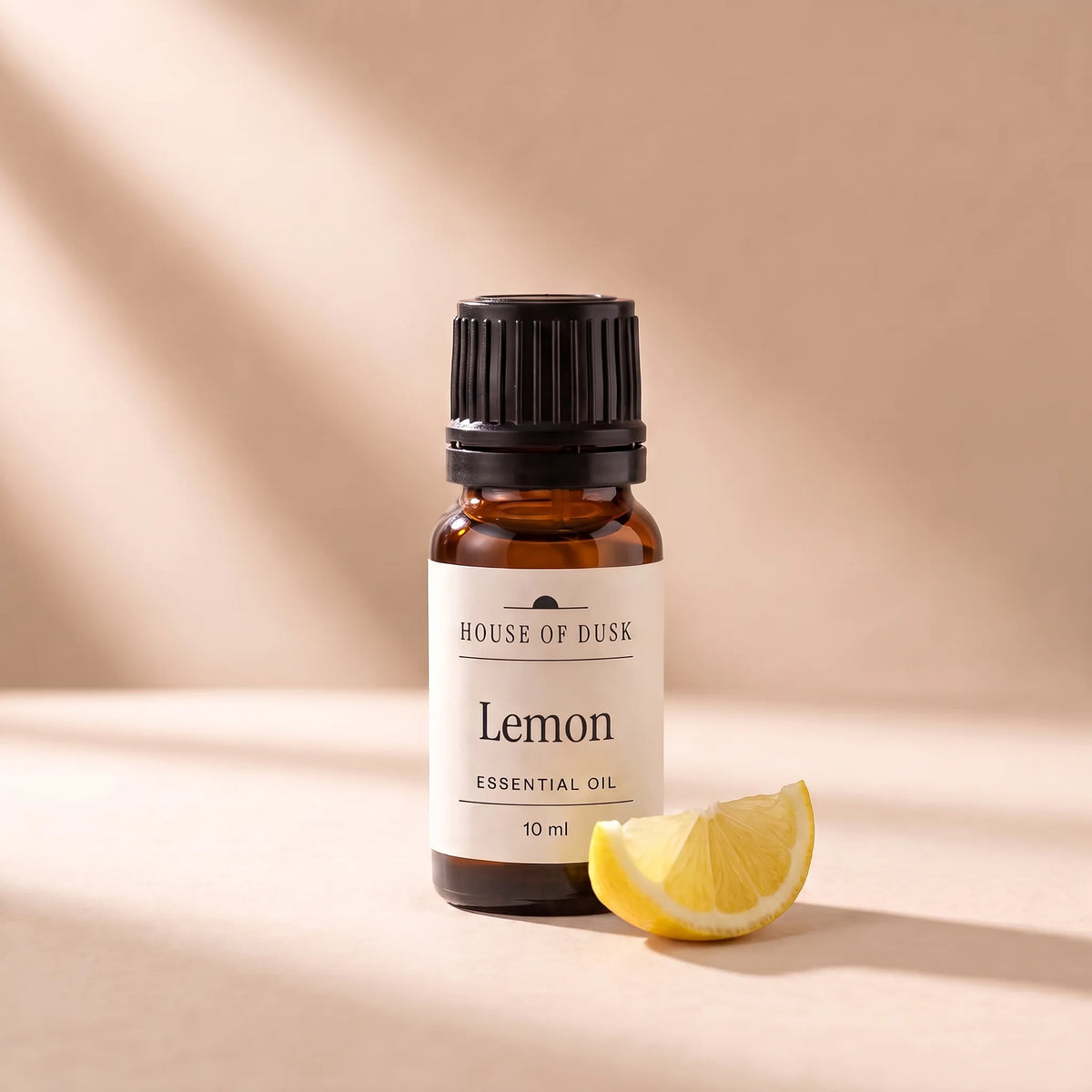 Lemon essential oil in a 10 ml amber glass bottle with a House of Dusk label, beside a small wedge of fresh lemon showing its yellow peel