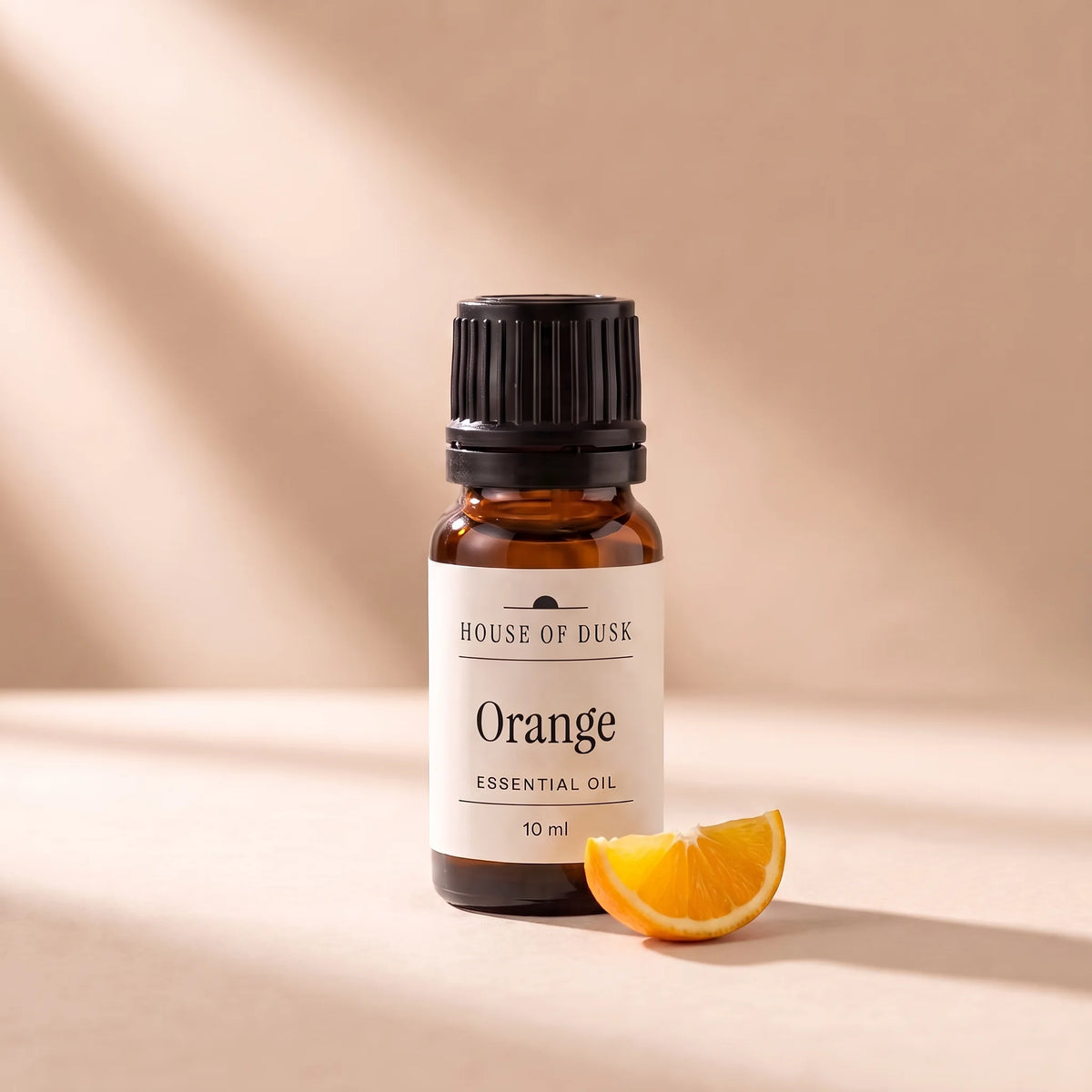 Orange essential oil in a 10 ml amber glass bottle with a House of Dusk label, beside a small slice of fresh orange