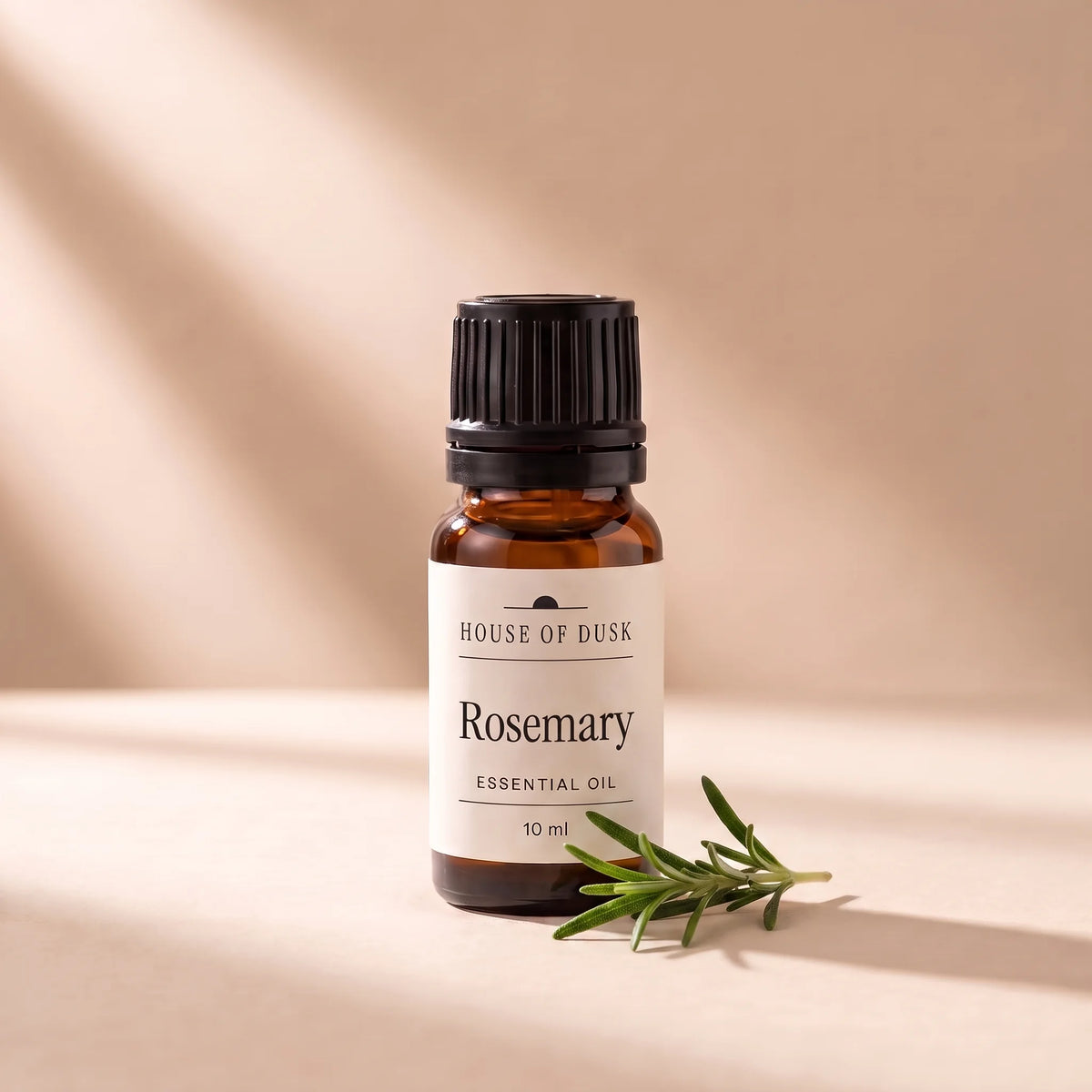Rosemary essential oil in a 10 ml amber glass bottle with a House of Dusk label, beside a small sprig of fresh rosemary