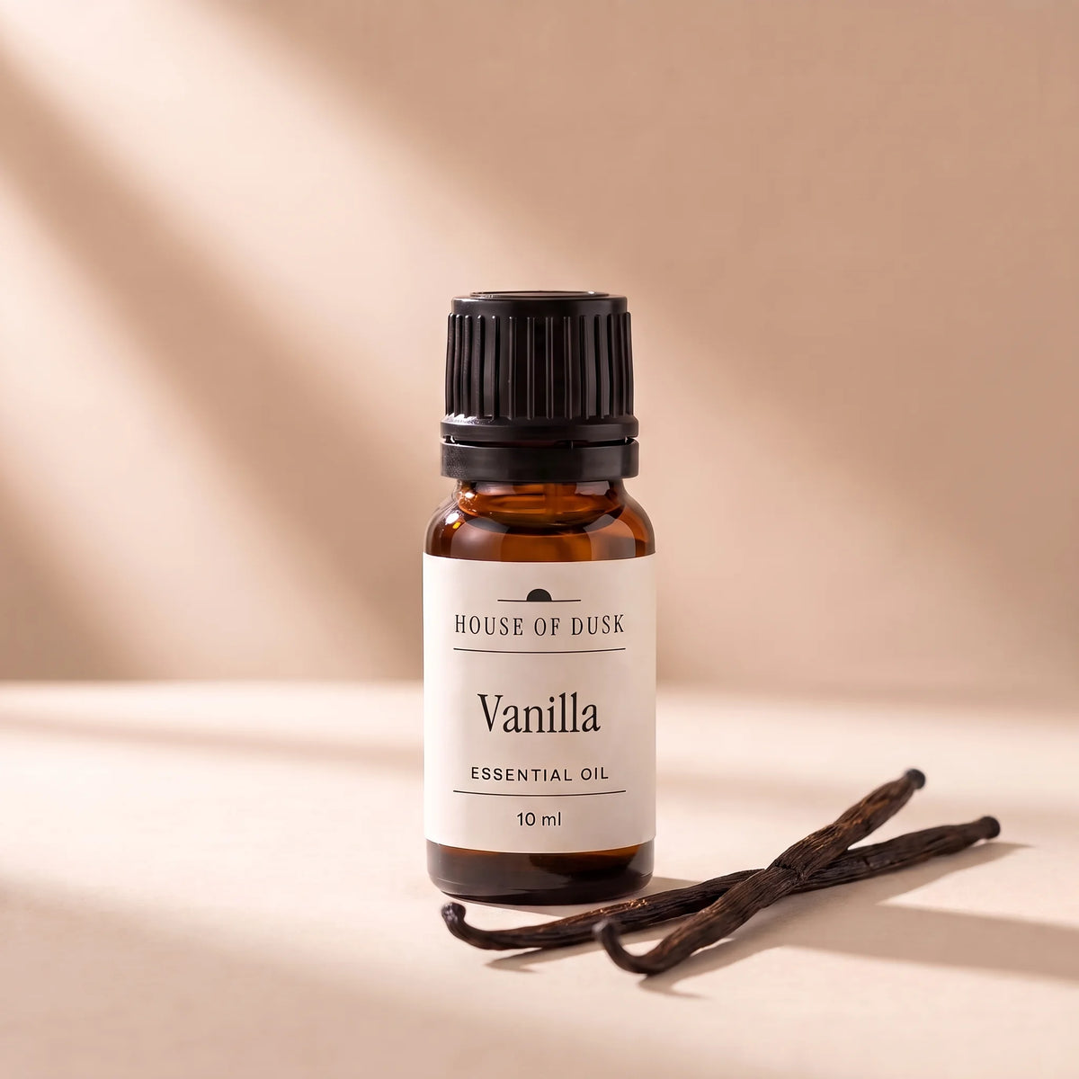 Vanilla essential oil in a 10 ml amber glass bottle with a House of Dusk label, beside two dark brown vanilla pods