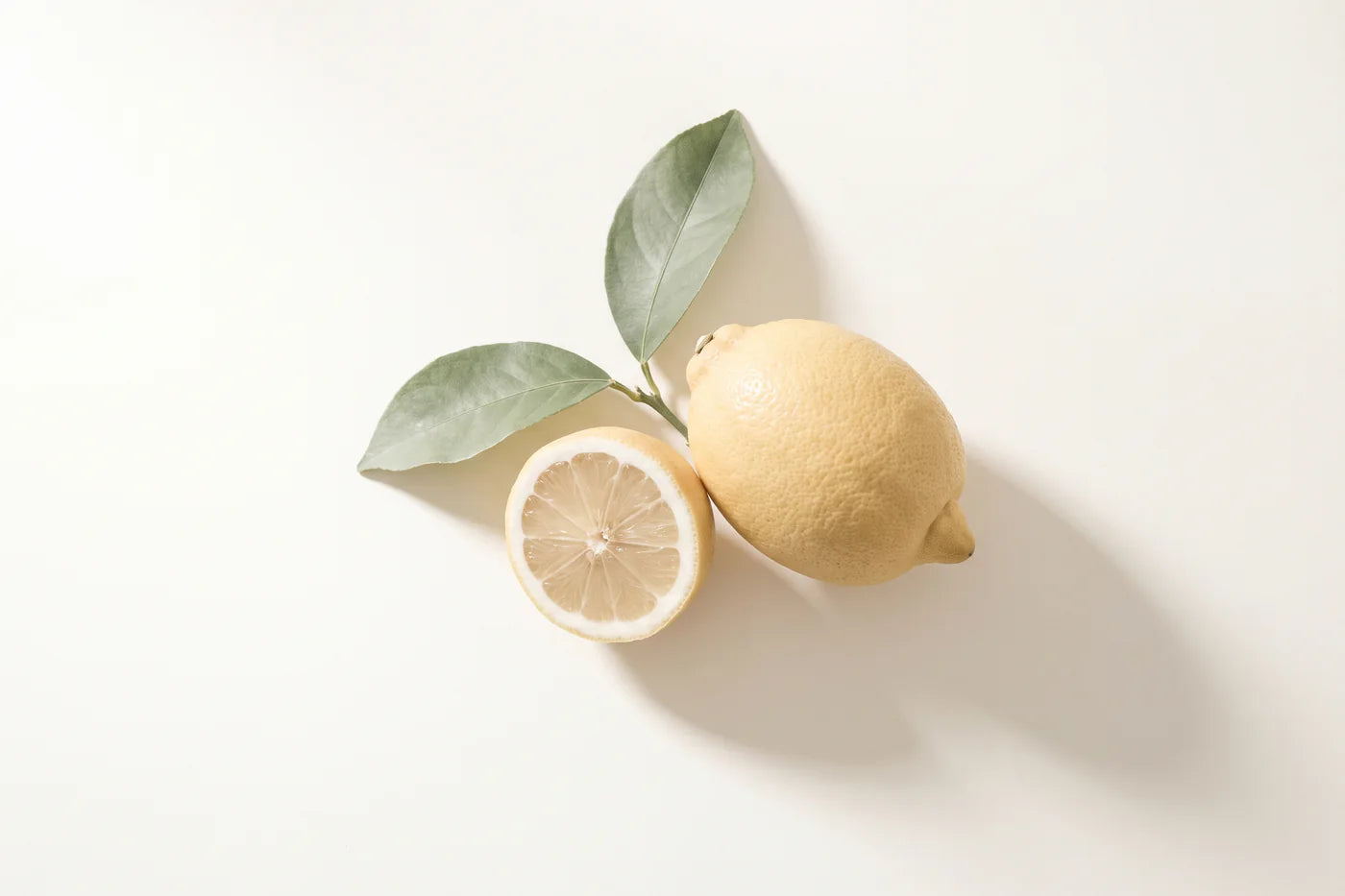 A whole lemon beside a cut half showing its segments, with a short sprig of two leaves.